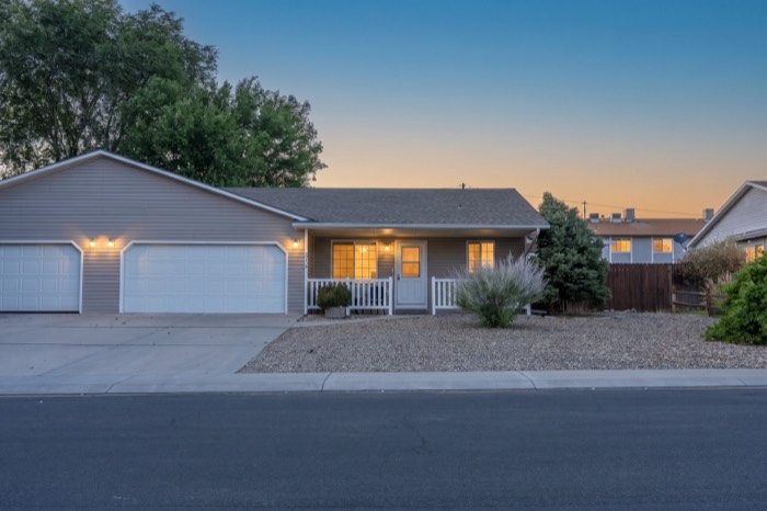 Twilight exterior of a Colorado residential listing with porch and garage lights on